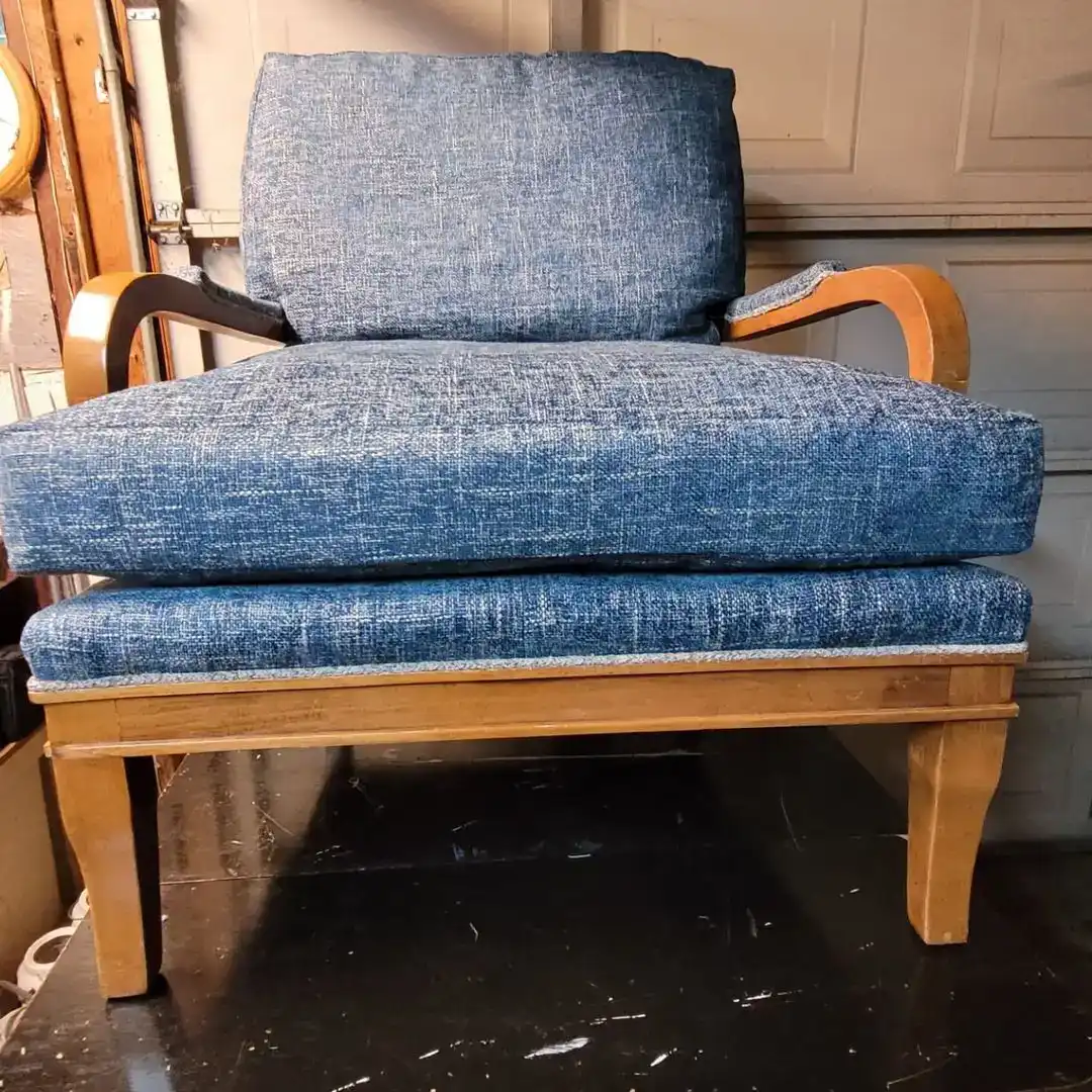 Front view of a wooden armchair with thick blue upholstered seat and back cushions and curved wood arms.