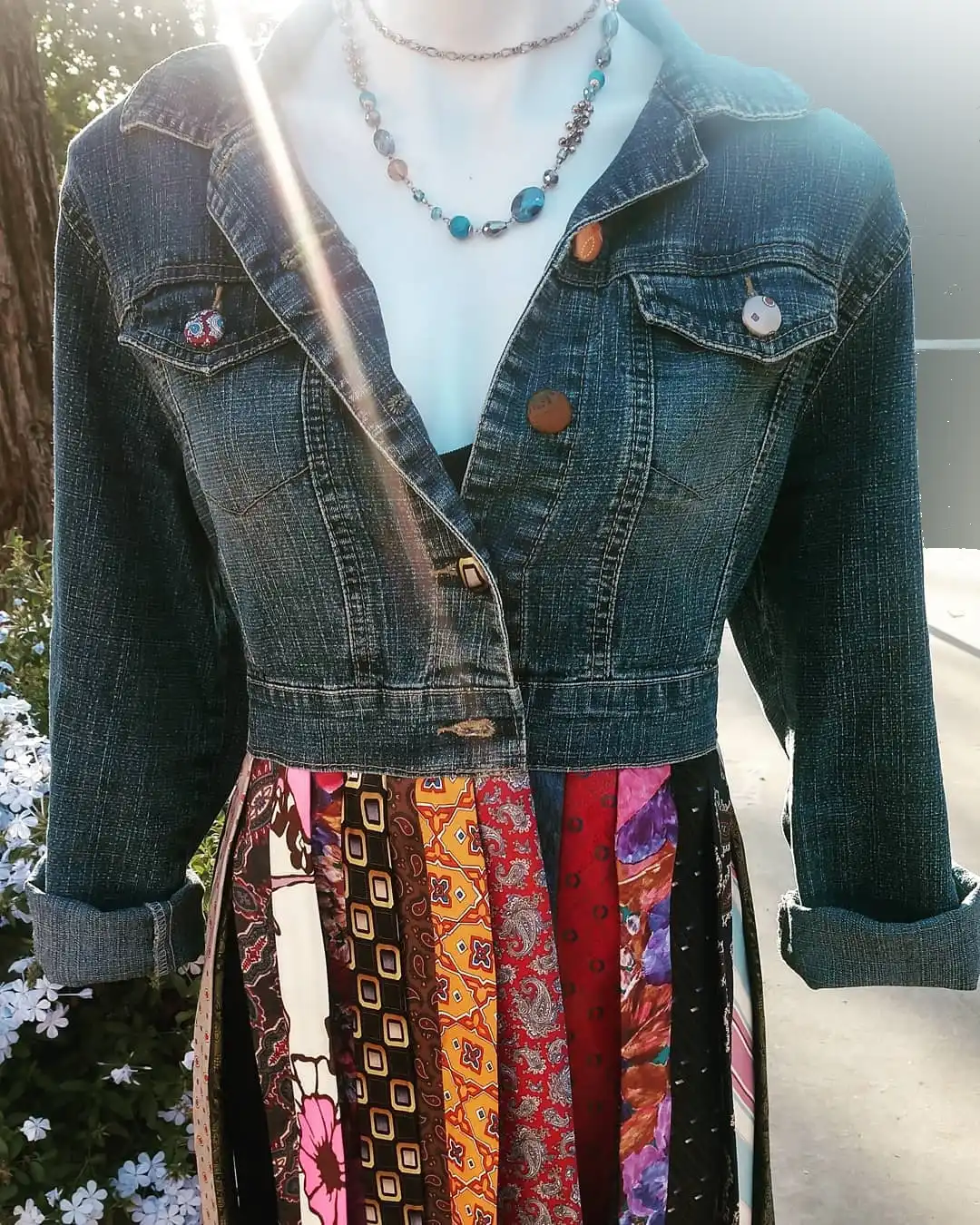 Close-up of denim jacket with buttons and beaded necklace over a patchwork tie skirt.
